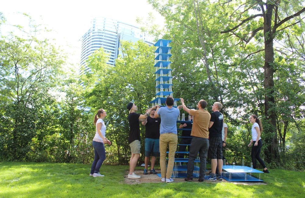 Menschen bauen einen hohen Turm aus Brettern Platten und Bechern, alle helfen zusammen