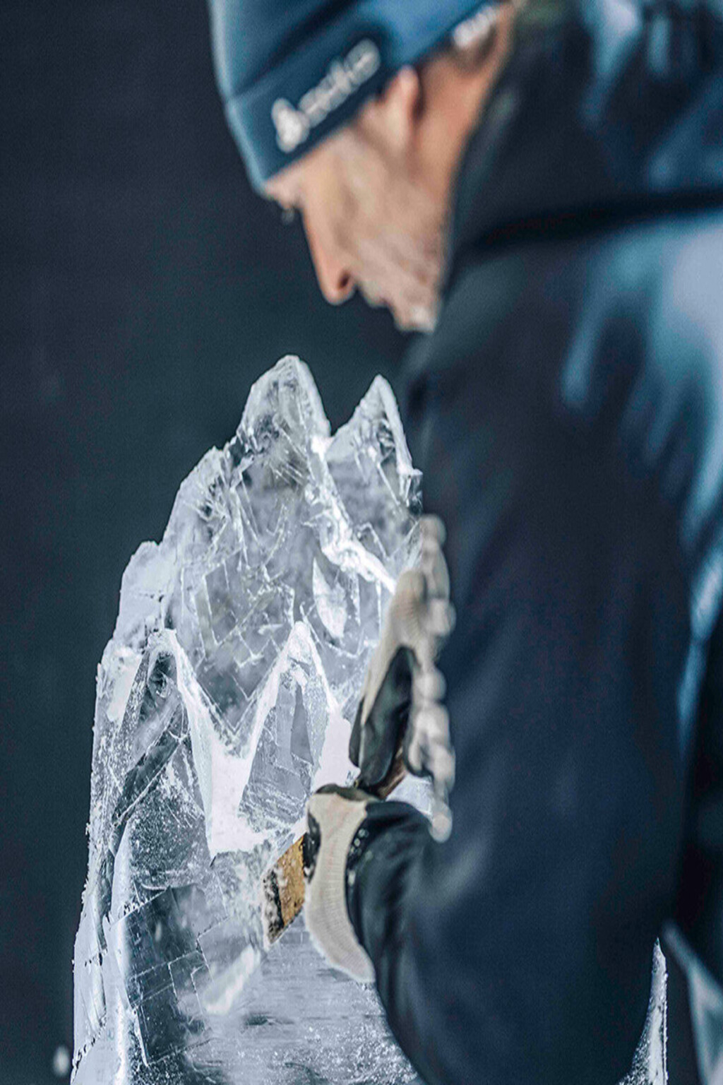 Ein Teilnehmer schnitzt konzentriert eine detailreiche Skulptur aus einem klaren Eisblock – kreative Teambuilding-Aktivität beim winterlichen Eisschnitzen während eines Firmen-Teamevents oder einer Weihnachtsfeier.