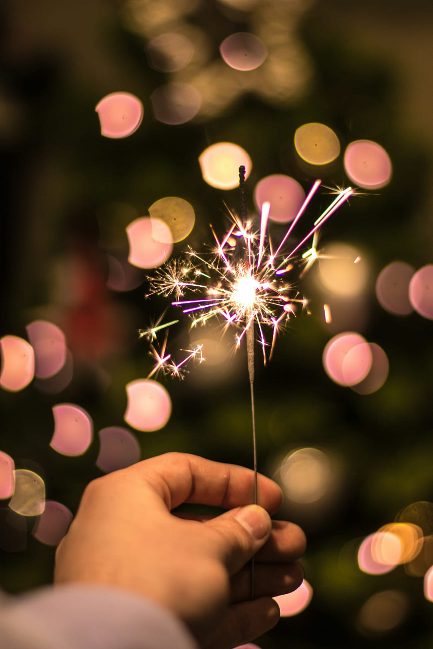 Hand hält eine leuchtende Wunderkerze vor festlich unscharfem Hintergrund – symbolisch für Feier, Teamspirit und besondere Teamevents im Winter.